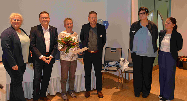 Mehrere Menschen, in der Mitte eine Frau mit Blumenstrauß.