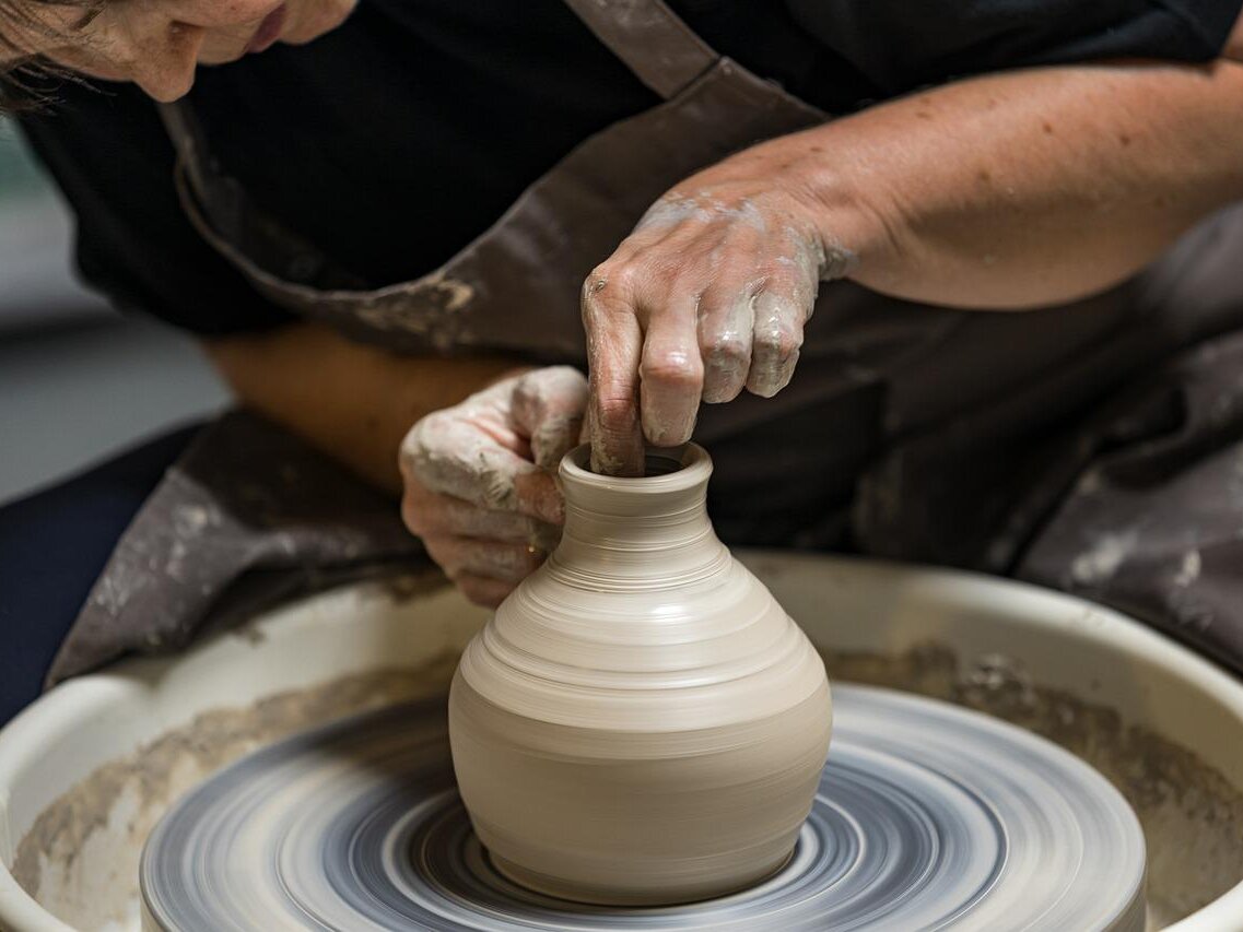 Eine Frau formt eine Vase aus Ton auf einer Töpferscheibe.