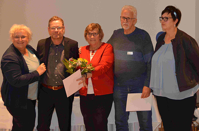 Mehrere Menschen, in der Mitte eine Frau und ein Mann mit Blumenstrauß und Urkunde.